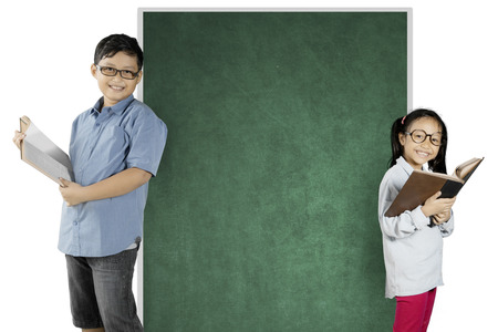 Two nerdy students reading a book while standing near a blank chalkboard, isolated on white backgroundの写真素材