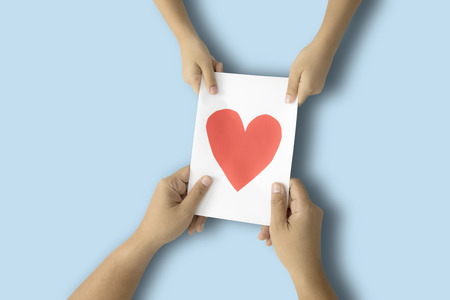 Father's Day. Hands of dad and child holding a greeting card with heart symbol, shot with blue backgroundの写真素材