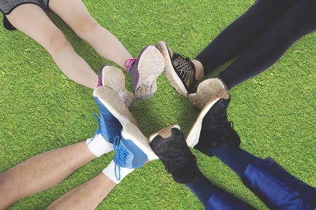 Top view of group of friends sitting on the green grass make foot circle with their legs and different shoes after workout togetherの写真素材