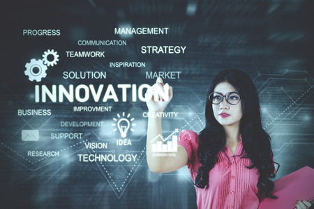 Image of pretty businesswoman holding a folder while writing a text of innovation on the virtual screenの写真素材