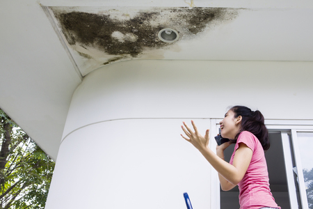 Picture of young woman looks angry while talking on the mobile phone with damaged ceilingの写真素材