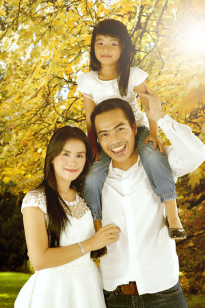 Young parents with her daughter smiling at the camera while playing together in the park, shot at autumn timeの写真素材