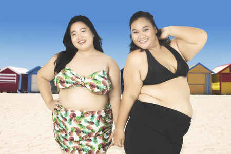 Two fat women look happy while wearing swimwear and standing near the cottageの写真素材