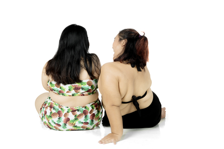 Back view of two fat women wearing swimwear while sitting in the studio, isolated on white backgroundの写真素材