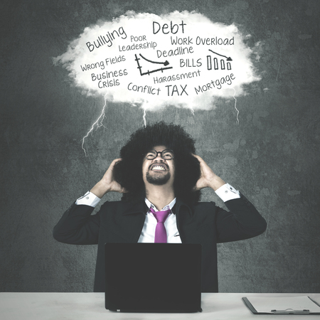 Image of stressful Afro businessman sitting with a laptop and clipboard while thinking his problemsの写真素材