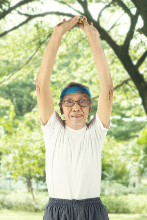 Portrait of an elderly man wearing sportswear while stretching his arm in the parkの写真素材