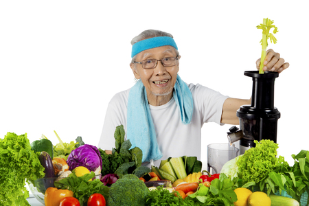 Picture of an elderly man wearing sportswear while making vegetable juice, isolated on white backgroundの写真素材