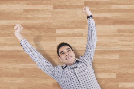 Top view of an Asian man looks relaxed while lying down on the wooden floorの写真素材