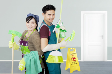 Image of two janitors holding cleaning equipment while standing in the hotelの写真素材