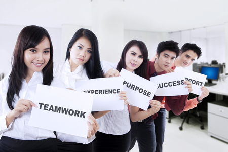 Young business people standing in the office while showing papers with different wordsの写真素材
