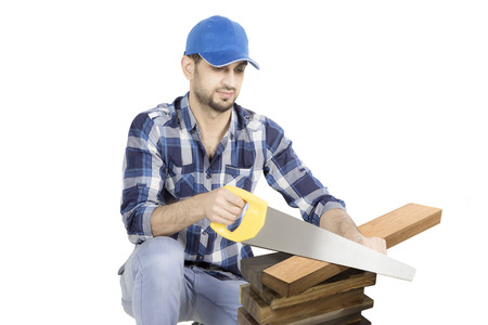 Italian man carpenter cutting a wood of plank with a hand saw while squatting in the studioの写真素材