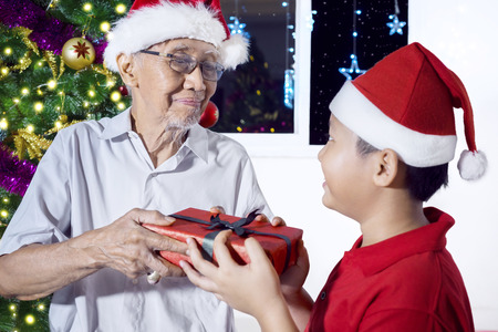 Image of an elderly man looks happy while receiving a Christmas gift from his grandson at homeの写真素材