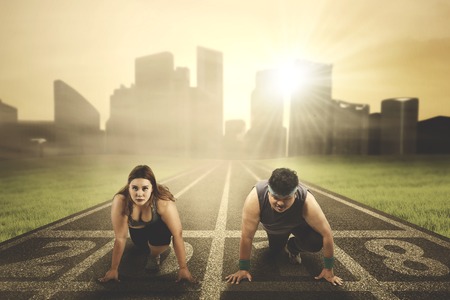 Image of young fat couple ready to compete while kneeling on the road with numbers 2018の写真素材