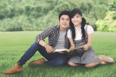 Photo of two college students looks happy while studying with a book and sitting in the parkの写真素材