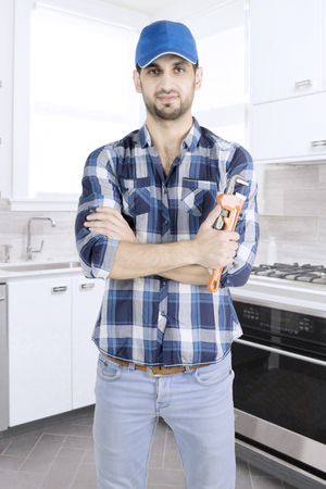 Portrait of Male plumber folded his hand while standing in the kitchen and holding a wrench の写真素材