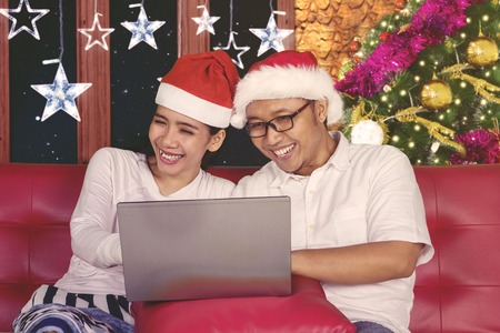 Image of happy couple using a laptop computer while sitting on the couch at Christmas timeの写真素材