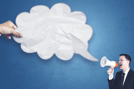 Portrait of young European businessman talking at empty cloud bubble through a megaphoneの写真素材