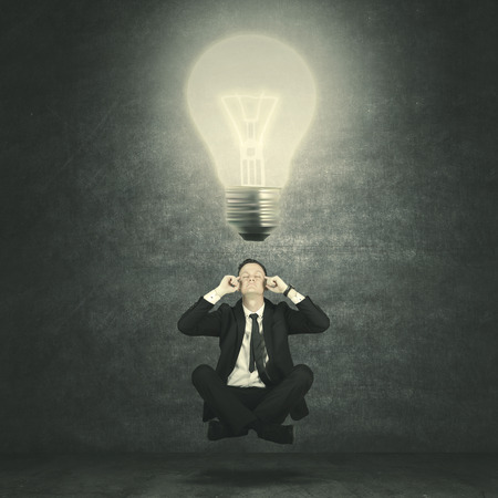 Picture of European businessman levitating under a bright bulb while thinking an ideaの写真素材