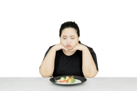 Image of fat woman looks unhappy while eating healthy food, isolated on white backgroundの写真素材