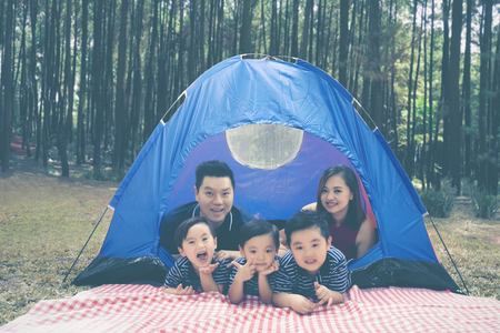 Picture of young family smiling at the camera while lying in the tent and camping in the forestの写真素材