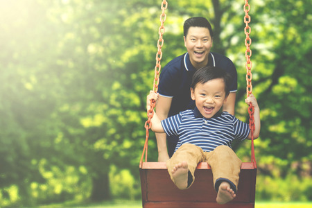 Image of young father pushing his son on the swing while having fun in the parkの写真素材