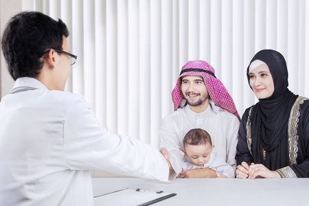 Portrait of Arab parents and their son shaking hands with a pediatrician while consultation in the hospitalの写真素材