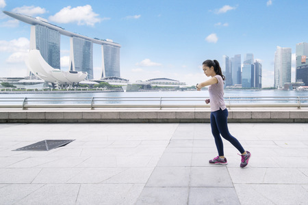 SINGAPORE, January 02, 2018: young woman looking at her wristwatch while running on the esplanade bridgeのeditorial素材