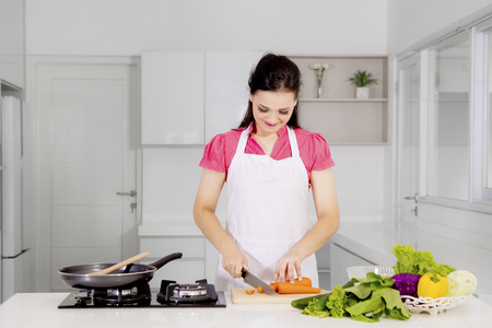 Picture of beautiful woman cutting a carrot while cooking in the kitchenの写真素材