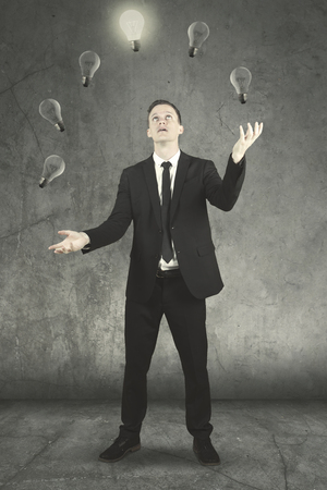 Portrait of American businessman wearing formal suit while juggling light bulbsの写真素材