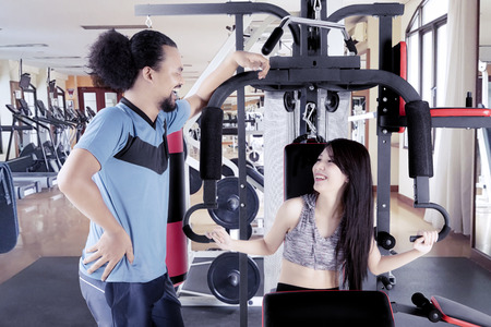 Beautiful woman laughing with her friend in the gym center while exercising with a weight machine
