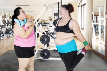 Picture of two fat women laughing together while doing a stretch in the fitness centerの写真素材