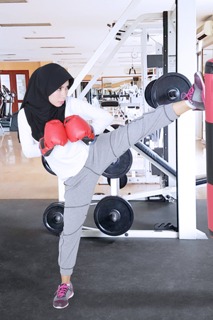 Muslim woman wearing sportswear and veil while kicking a boxing sack. Shot in the gym centerの写真素材