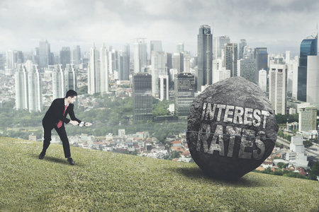 Picture of Italian businessman pulling a rock with text of interest rates while climbing on the hillの写真素材