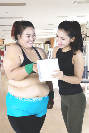 Portrait of obese woman with her trainer looking at a digital tablet after workout in the gym centerの写真素材