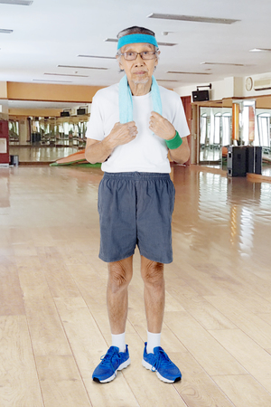 Full length of old man is wearing sportswear while standing in the fitness centerの写真素材