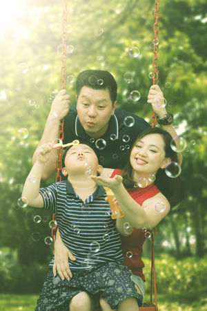 Portrait of happy family blowing soap bubbles while playing together in the playground の写真素材