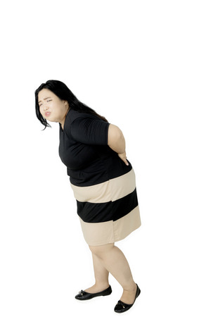 Portrait of obese woman having backache while standing in the studio, isolated on white backgroundの写真素材
