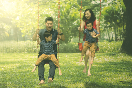 Image of young parents and their sons look happy while playing swings in the parkの写真素材