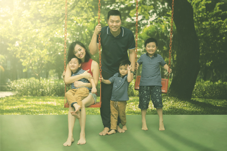 Picture of young parents smiling at the camera while playing with their three sons in the playgroundの写真素材