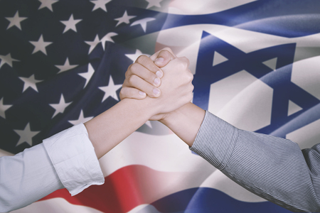 Closeup of two business people shaking hands after deal business with America and Israel flag in the backgroundの写真素材