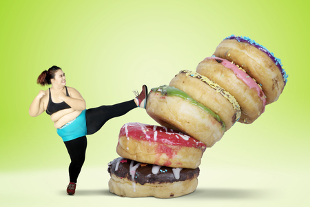 Overweight young woman kicking donuts while wearing sportswear. Shot with green screen backgroundの写真素材