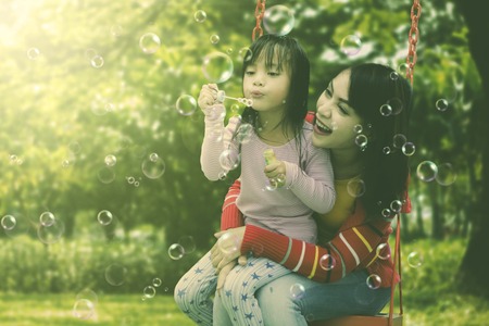 Mother and daughter having fun blowing soap bubbles at parkの写真素材