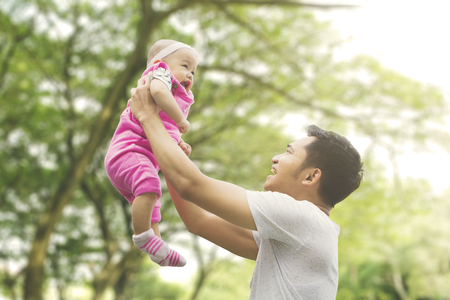 Asian family spending spring concept: a father lifting daughter with blur tree backgroundの写真素材