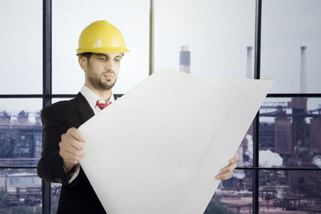 Young male architect read the blue print near the office windowの写真素材