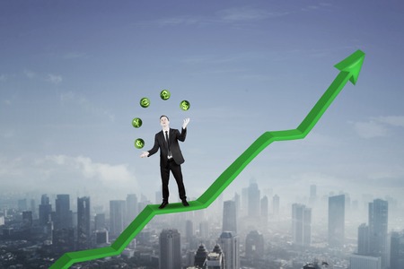 American businessman juggling with currency symbols while standing on an upward arrowの写真素材