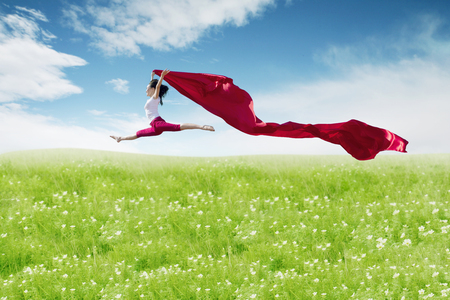 Asian woman ballerina holding red fabric making a big jump on blossom meadow. Summer or Spring conceptの写真素材