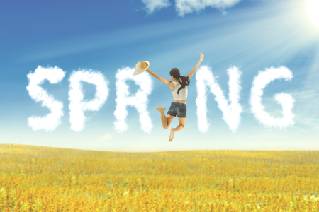 Happy Asian woman holding hat jumping on meadow. Summer or spring conceptの写真素材