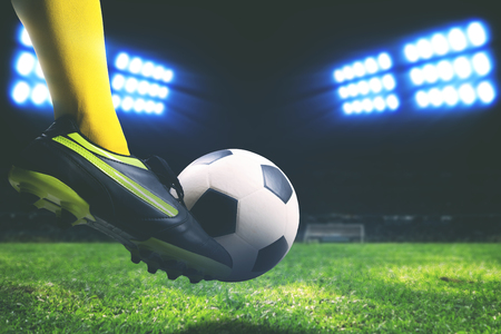 Closeup of foot kicking soccer ball on soccer field inside a stadium at nightの写真素材