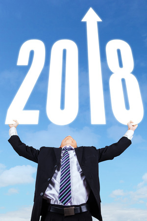 Portrait of young businessman holding numbers 2018 with upward arrow 