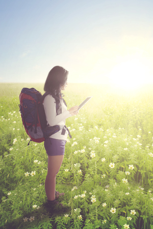 Portrait of young tourist woman using a digital tablet while standing on the blossom meadowの写真素材